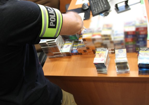 policjant zabezpiecza odzyskane z włamania wyroby tytoniowe