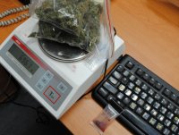 na biurku stoi elektroniczna waga, na niej marihuana w woreczkach strunowych. Obok widać klawiaturę i tester narkotykowy.