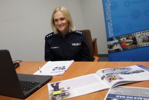 policjantka patrzy w monitor laptopa, za nią policyjny baner w kolorze niebieskim