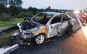 Zdjęcie przedstawia spalony pojazd, po uderzeniu w bariery ochronne.