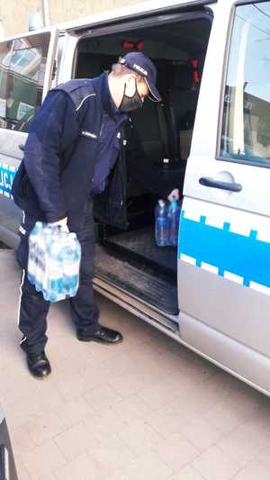Zdjęcie przedstawia policjnata, pakującego wodę do radiowozu.