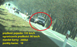 Zdjęcie przedstawia samochód koloru czarnego, który przekroczył prędkość o 65 km/h.