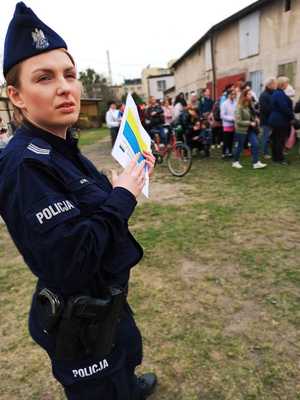 Zdjęcie przedstawia policjantkę stojącą z ulotkami, w tel widać uchodźców.