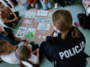 Zdjęcie przedstawia policjantkę, która razem z dziećmi omawia zasady dbania o środowisko.