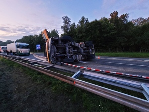 Zdjęcie przedstawia przewróconą ciężarówkę na autostradzie.