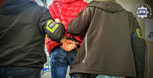 Zdjęcie przedstawia dwóch mężczyzn prowadzących zatrzymanego w kajdankach.