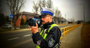 Zdjęcie kolorowe przedstawiające policjanta mierzącego prędkość pojazdów.