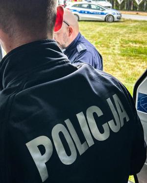 Zdjęcie przedstawia policjantów, w tle radiowóz.