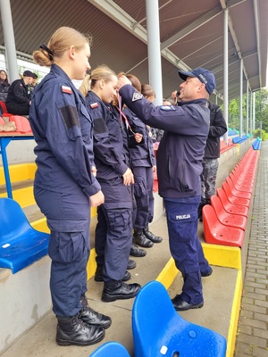 Zdjęcie kolorowe przedstawiające policjanta wręczającego medale uczniom klas mundurowych.