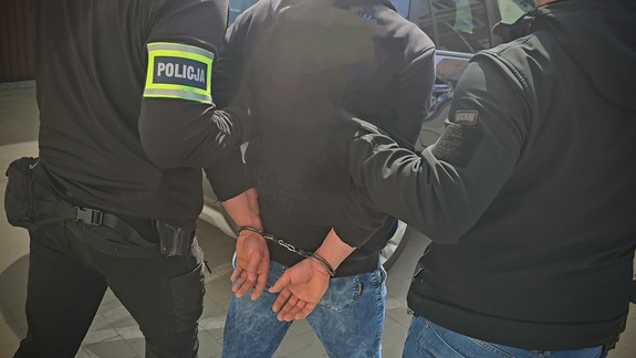 Zdjęcie kolorowe przedstawiające zatrzymanego prowadzonego przez policjantów kryminalnych.