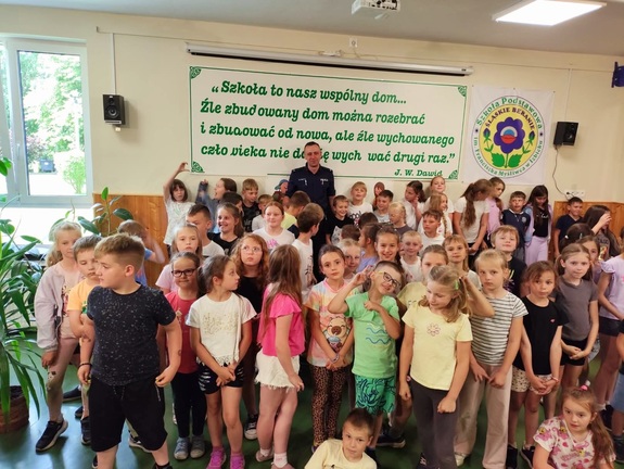 Zdjęcie kolorowe przedstawiające policjanta z dziećmi na spotkaniu edukacyjnym.