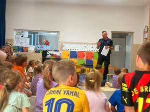 Zdjęcie kolorowe przedstawiające policjanta z dziećmi na spotkaniu edukacyjnym.