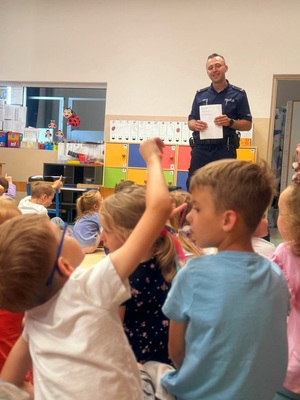 Zdjęcie kolorowe przedstawiające policjanta z dziećmi na spotkaniu edukacyjnym.