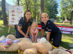 Zdjęcie kolorowe przedstawiające policjantki uczące dzieci przedszkolne pierwszej pomocy.