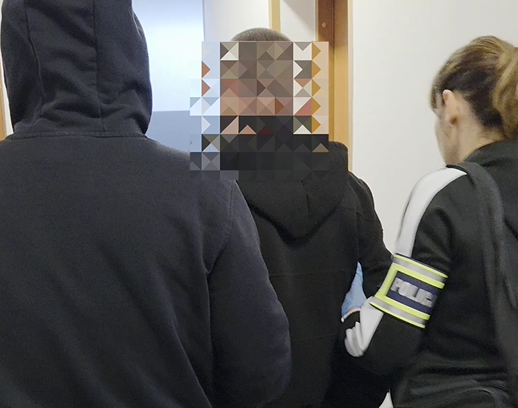 Zdjęcie kolorowe przedstawiające policjantów prowadzących zatrzymanego.
