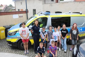 Zdjęcie kolorowe przedstawiające policjantów z dziećmi na spotkaniu w ramach programu &quot;Kręci mnie bezpieczeństwo w lecie&quot;.