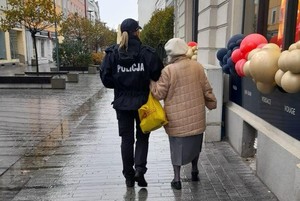 Zdjęcie kolorowe przedstawiające policjantkę idąca pod rękę z seniorką