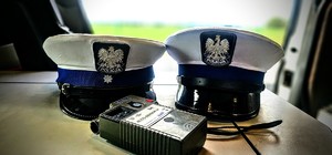Zdjęcie przedstawia dwie policyjne czapki i alkomat.