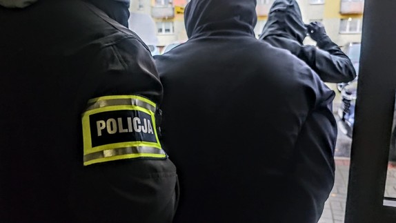 Zdjęcie przedstawia osobę zatrzymaną w asyście policjantów kryminalnych.