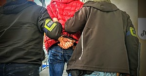 Zdjęcie przedstawia zatrzymanego prowadzonego przez policjantów kryminalnych.