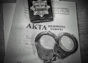 Zdjęcie przedstawia kajdanki, odznakę i akta.