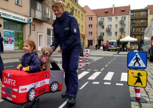 mała dziewczynka pod okiem policjantki pokonuje trasę miasteczka ruchu drogowego w specjalnym samochodziku