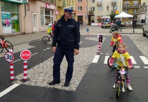 policjant nadzoruje małych rowerzystów jeżdżących po trasie miasteczka ruchu drogowego