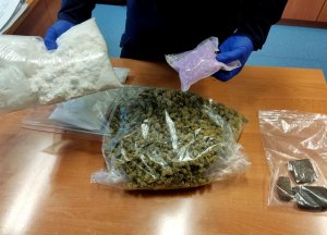 policjant trzyma w rękach tabletki ekstazy oraz marihuanę
