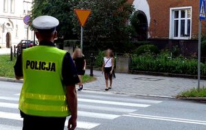 policjant ruchu drogowego nadzoruje oznakowane przejście dla pieszych w rejonie szkoły
