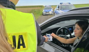 policjantka i kierująca samochodem, policjantka wręcza kobiecie naklejkę z napisem zwolnij mistrzu