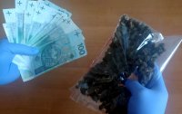 policjant trzyma w dłoniach zabezpieczone pieniądze oraz marihuanę