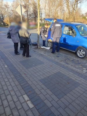 Zdjęcie przedstawia policjantów wymieniających koło w samochodzie.