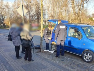 Zdjęcie przedstawia policjantów wymieniających koło w samochodzie.