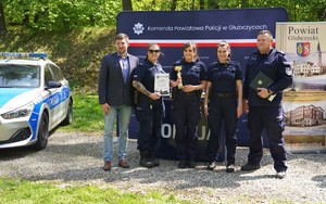 Policjantki stoją w rzędzie z pucharem, obok radiowóz.