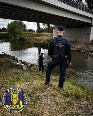 Zdjęcie; policjanci patrolują teren obok rzeki.