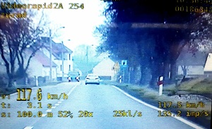 widok z ekranu wideorejstratora, samochodu nieoznakowanego policji, na ekranie widoczny liczby wskazujące prędkość oraz inne parametry,widoczny również w oddali samochód osobowy, jezdnia,zabudowania i drzewa