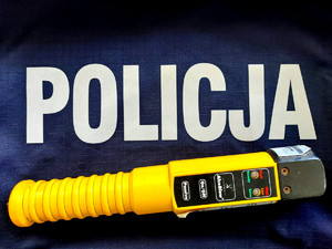 Obraz przedstawia urządzenie do badania zawartości alkoholu w wydychanym powietrzu, który jest położony na bluzie z napisem &quot;Policja&quot;