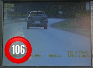 Obraz jest kolorowy, przedstawia pojazd w oddali. W lewym dolnym rogu pojawia się liczba 106, która określa prędkość z jaką porusza się samochód.