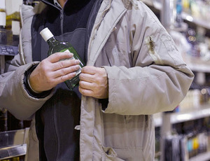 Na obrazu znajduje się sylwetka osoby, która chowa butelkę alkoholu pod kurtką.