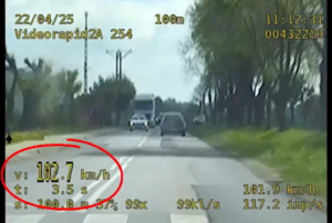 Obraz przedstawia zrzut ekranu z wideorejestratora. Na jego wyświetlaczu pojawia się w oddali pojazd Seat, a z lewej strony na dole znajduje się prędkość określona 102 kilometry na godzinę.