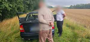 zdjęcie przedstawia dwóch mężczyzn w kajdankach, którzy stoją obok samochodu