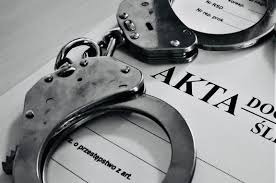 na zdjęciu znajdują się kajdanki ułożone na teczce z aktami dochodzeniowo-śledczymi