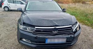 Zdjęcie przedstawia uszkodzony pojazd, który brał udział w kolizji. Pojazd jest koloru czarnego i ma widoczne uszkodzenia karoserii w przedniej części.