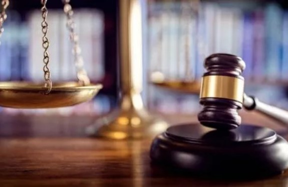 Obraz przedstawia młotek sędziowski. W tle znajduje się waga