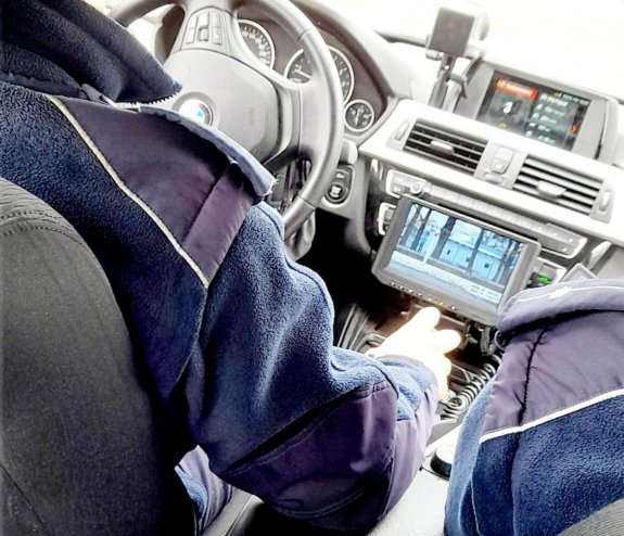 dwaj policjanci w radiowozie, deska rozdzielcza samochodu, kierownica, monitor wideorejestratora