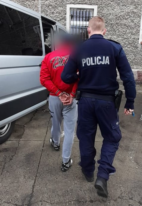 policjant, samochód koloru srebrnego, zatrzymany mężczyzna w czerwonej kurtce i szarych spodniach