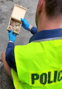Policjant w kamizelce odblaskowej trzymajacy w ręku pudełko drewniane z biżuterią