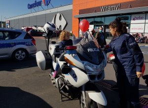 Policjantka wręcza dziewczynce siedzącej na motocyklu balona