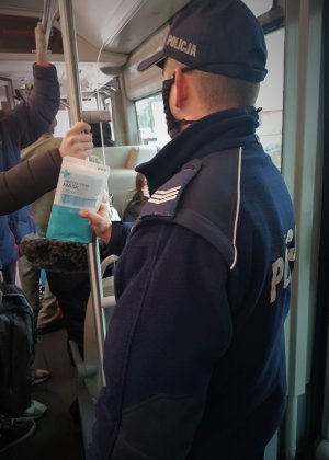 umundurowany policjant w autobusie. w ręce trzyma maseczki