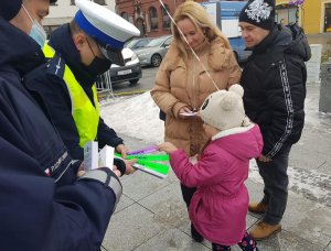 Policjanci podczas świątecznego jarmarku wręczają mieszkańcom opaski odblaskowe i zawieszki do prezentów